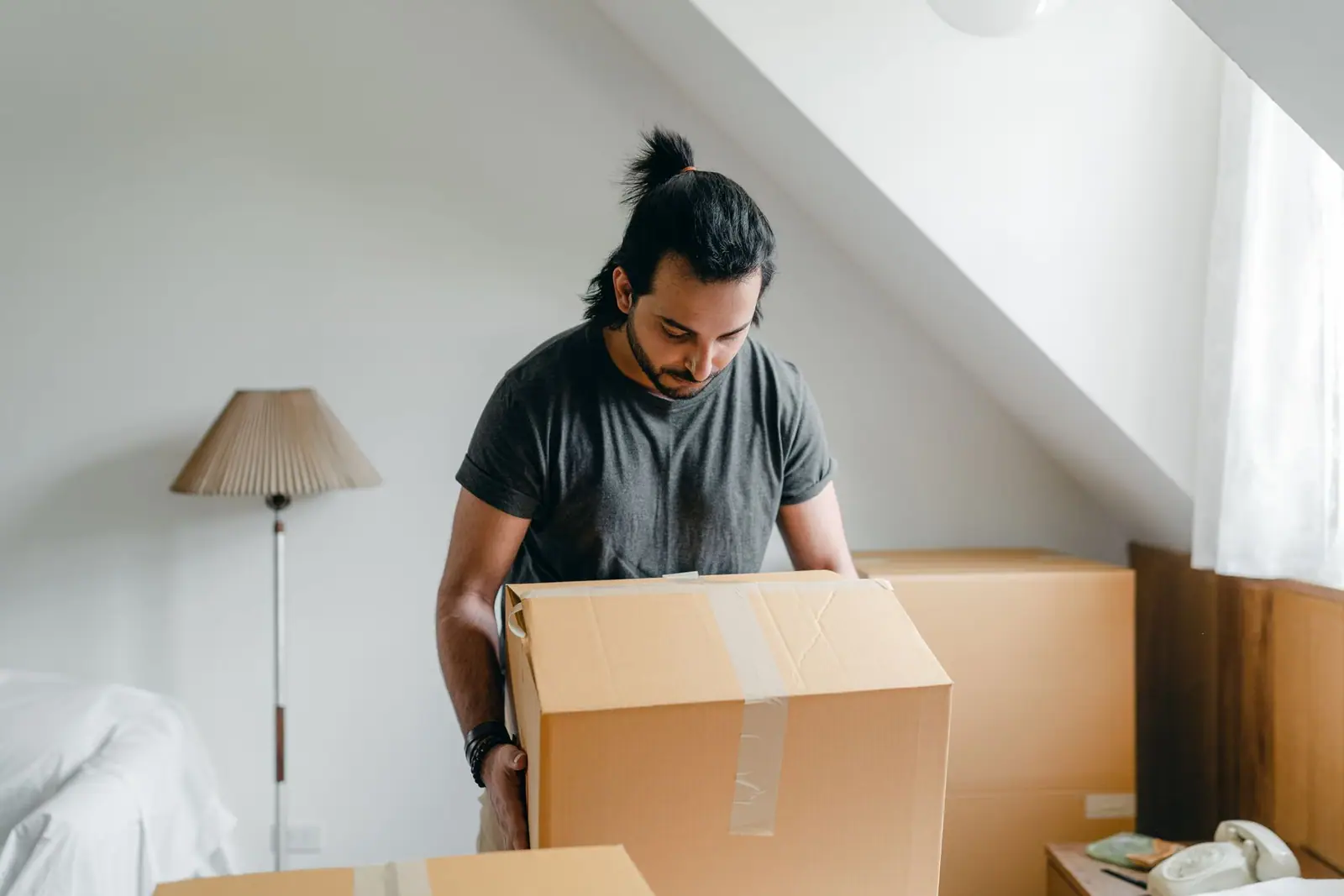 A man lifting a cardboard box in an attic room with a sloped ceiling