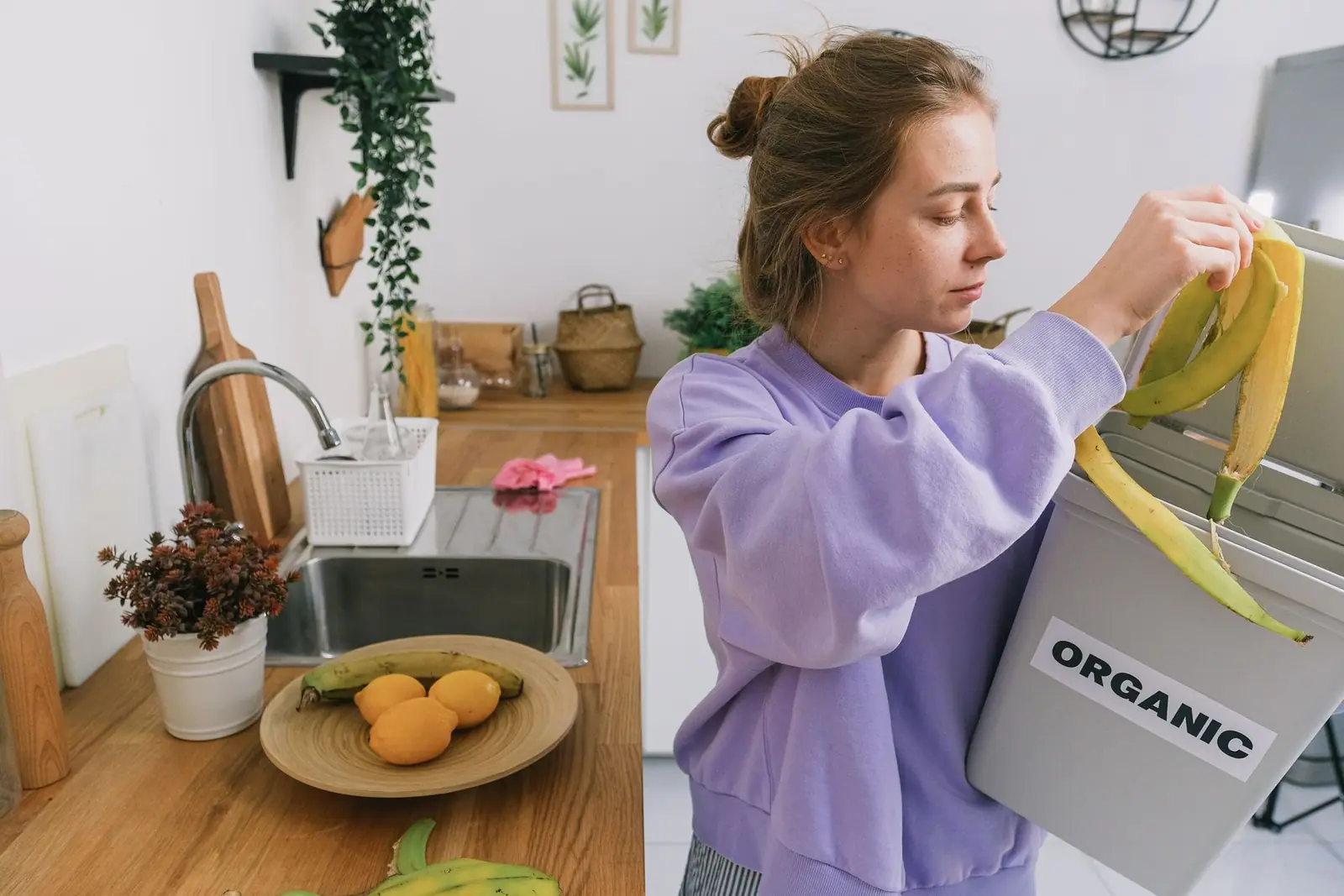 A woman dropping a banana peel into an organic waste bin in her kitchen