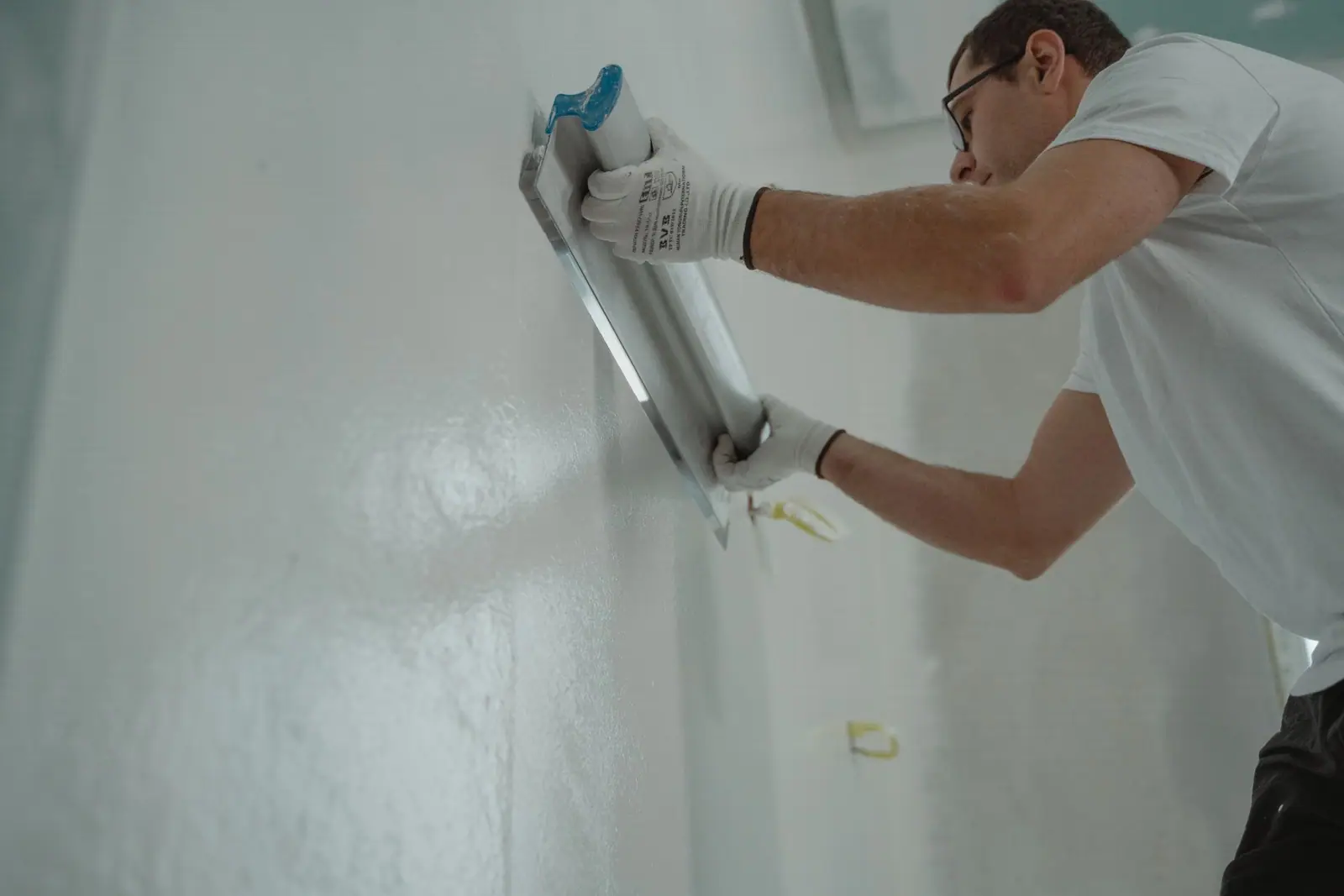 A worker smoothing material on an interior wall with a wide tool