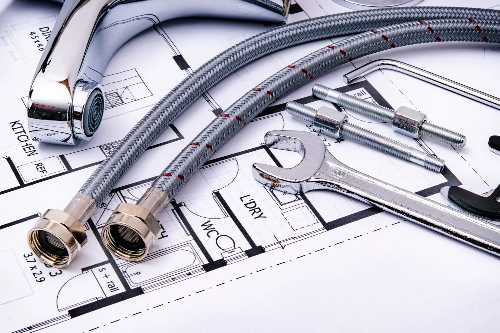 A faucet, braided supply hoses and plumbing tools arranged on a drawing