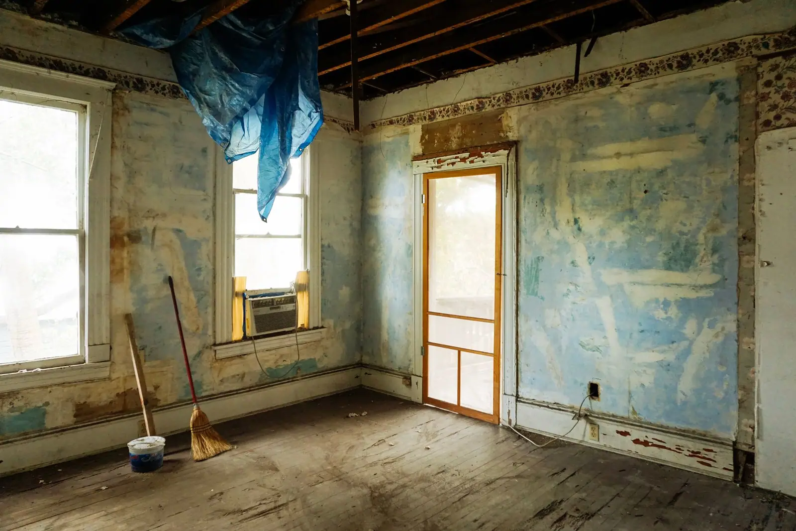 An unfinished room with stripped wall surfaces, exposed ceiling framing and tools