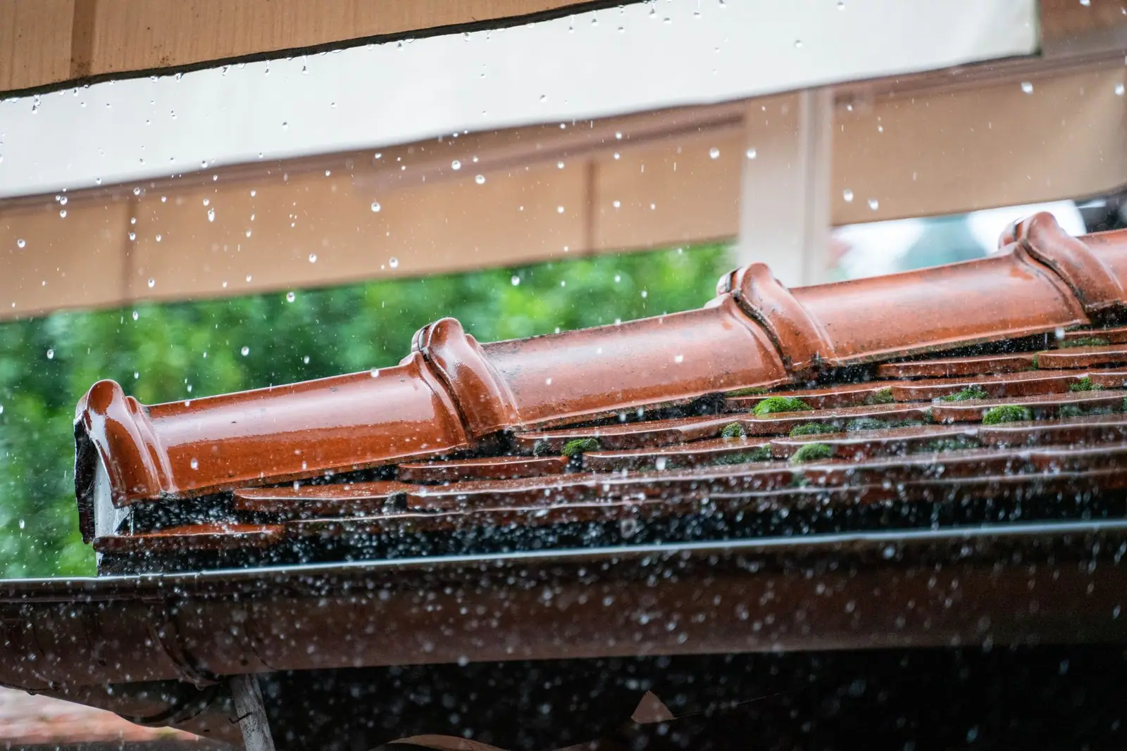 Rain falling beside roof tiles and a copper gutter