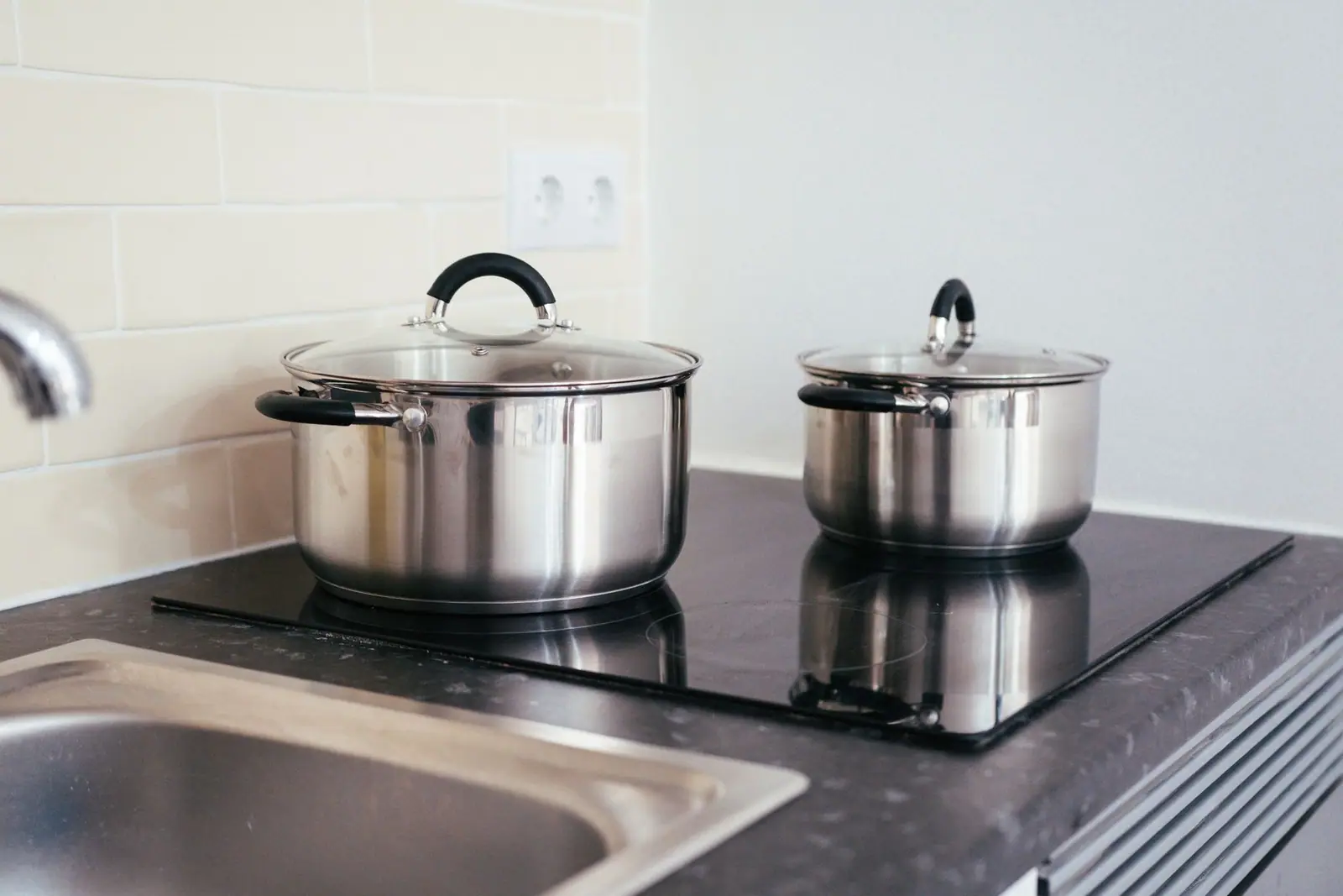 Stainless steel pots on a black glass cooking surface beside a tiled wall