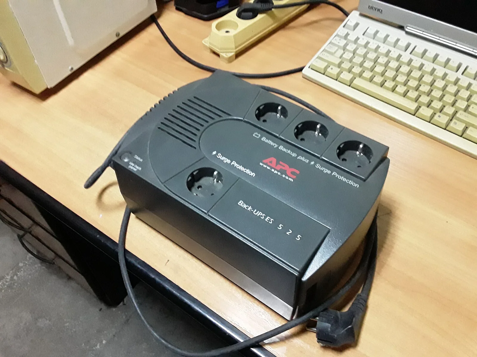 A black APC Back-UPS unit with battery-backup and surge-protection outlets beside a keyboard