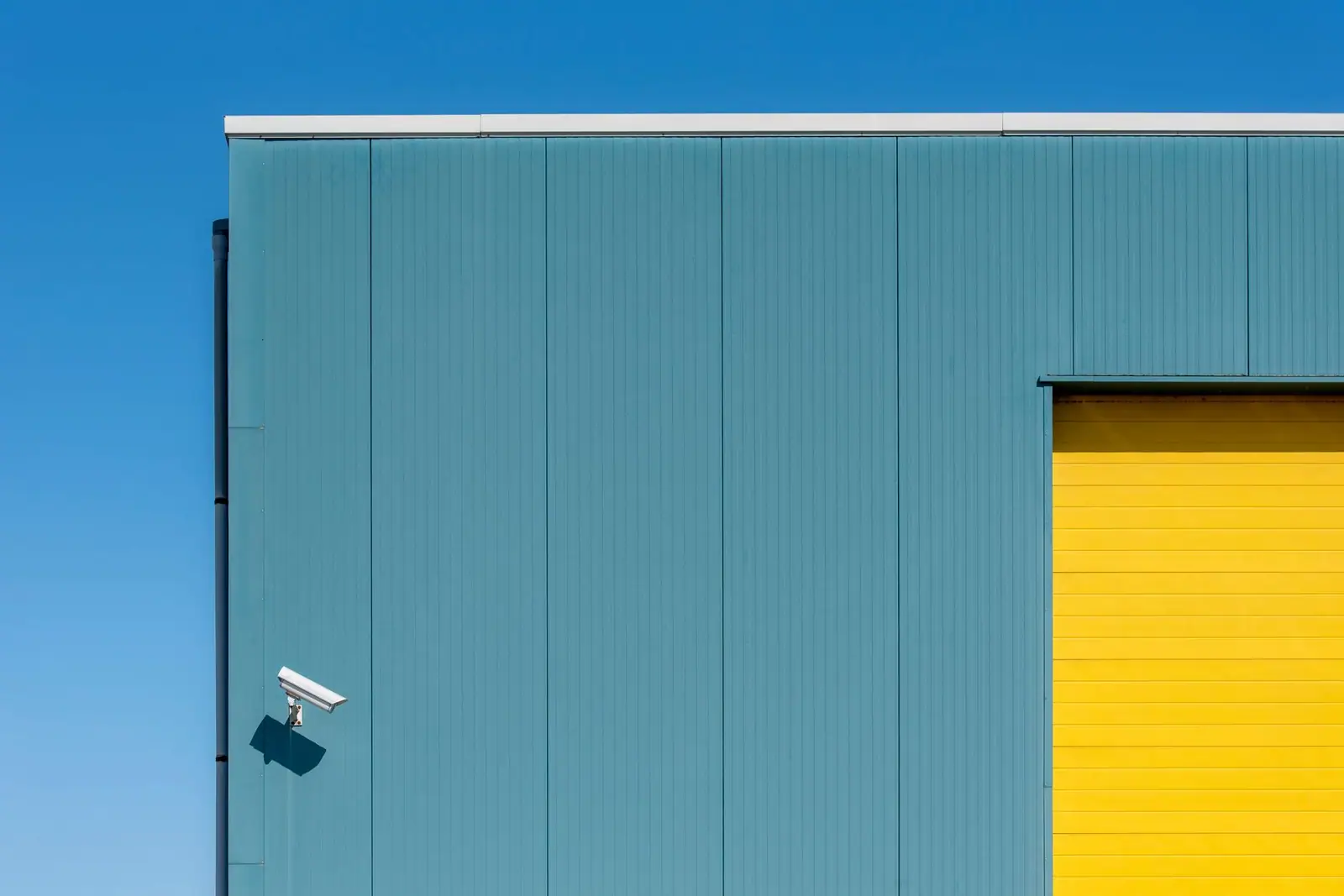 A white security camera mounted on a blue building above a yellow doorway