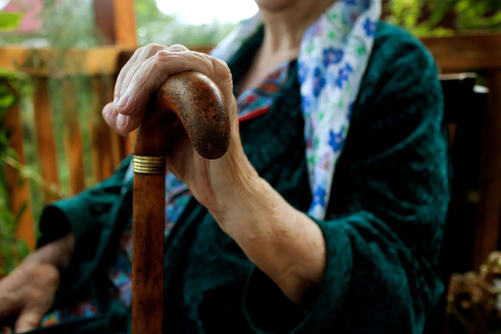 An older person's hands resting on the handle of a walking stick