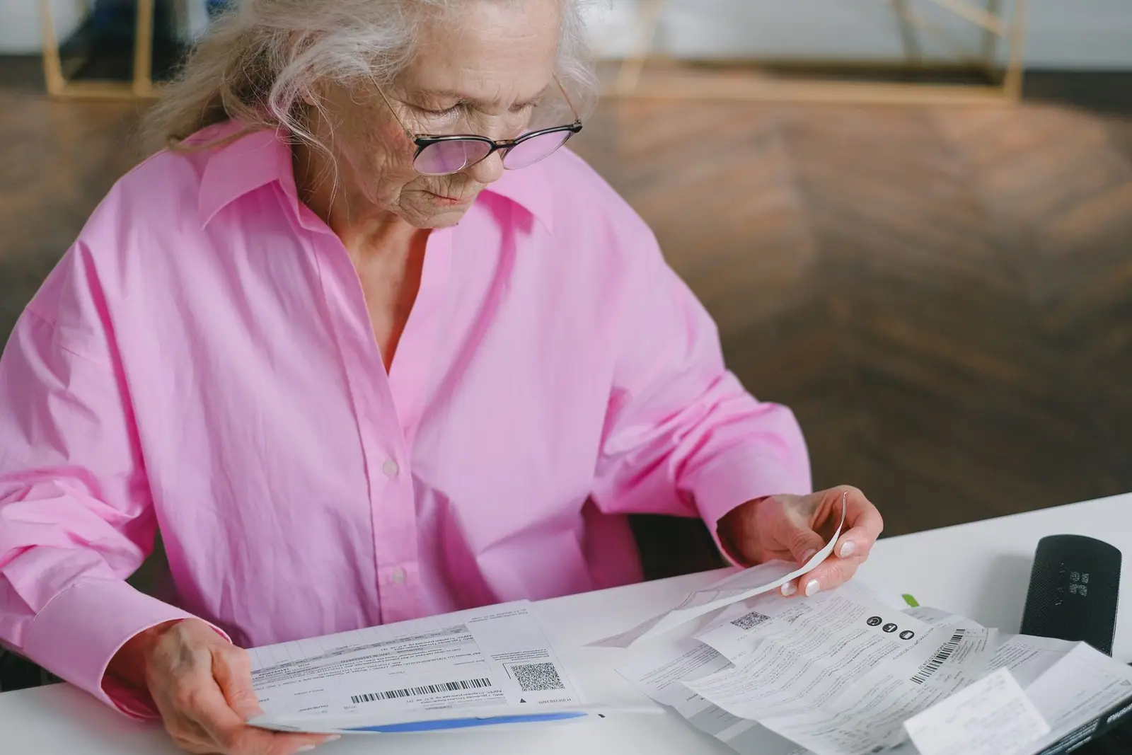 An older woman reading a printed document at a desk