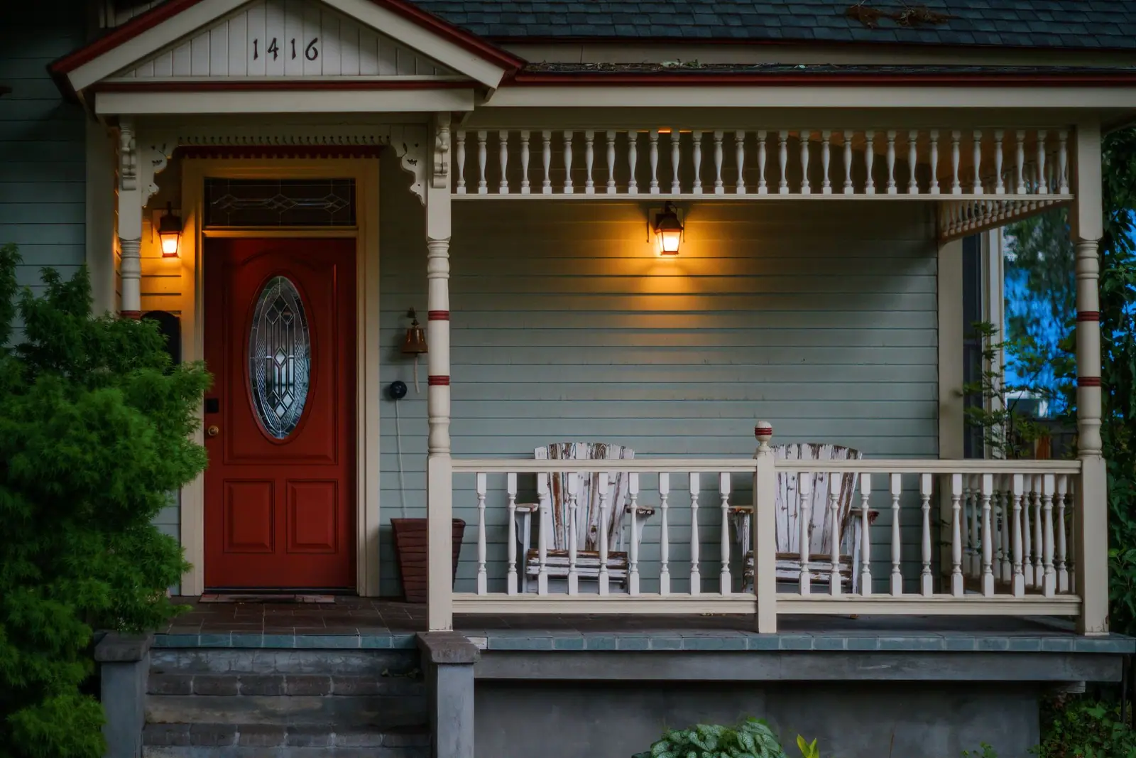 A porch with steps leading up to a red front door, lit in the evening