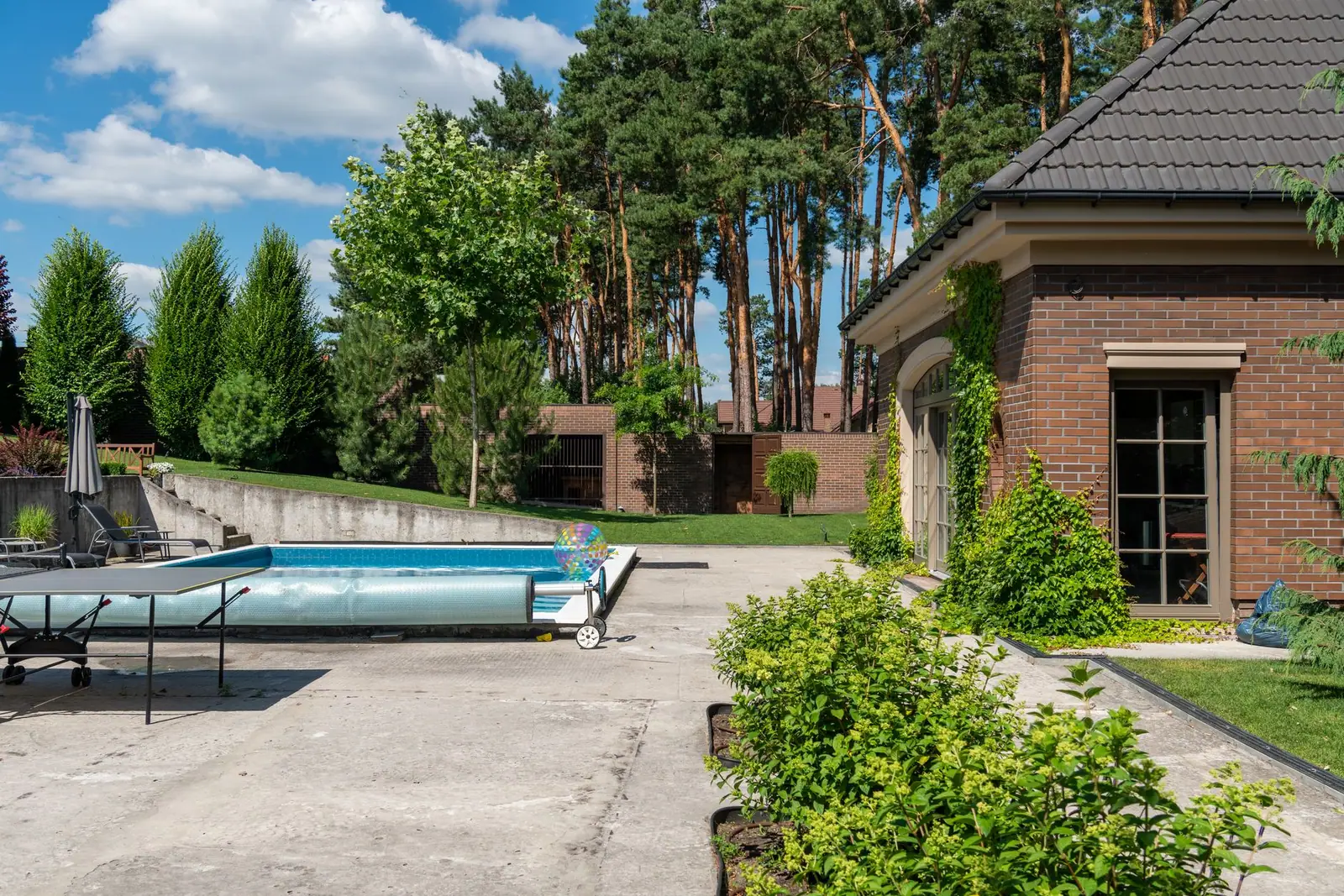 A backyard swimming pool beside a brick house with a cover reel at one end