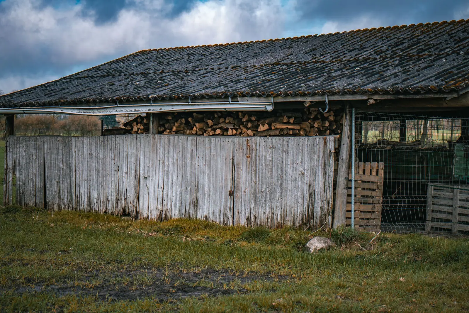 Firewood stacked under the eaves of a wooden barn