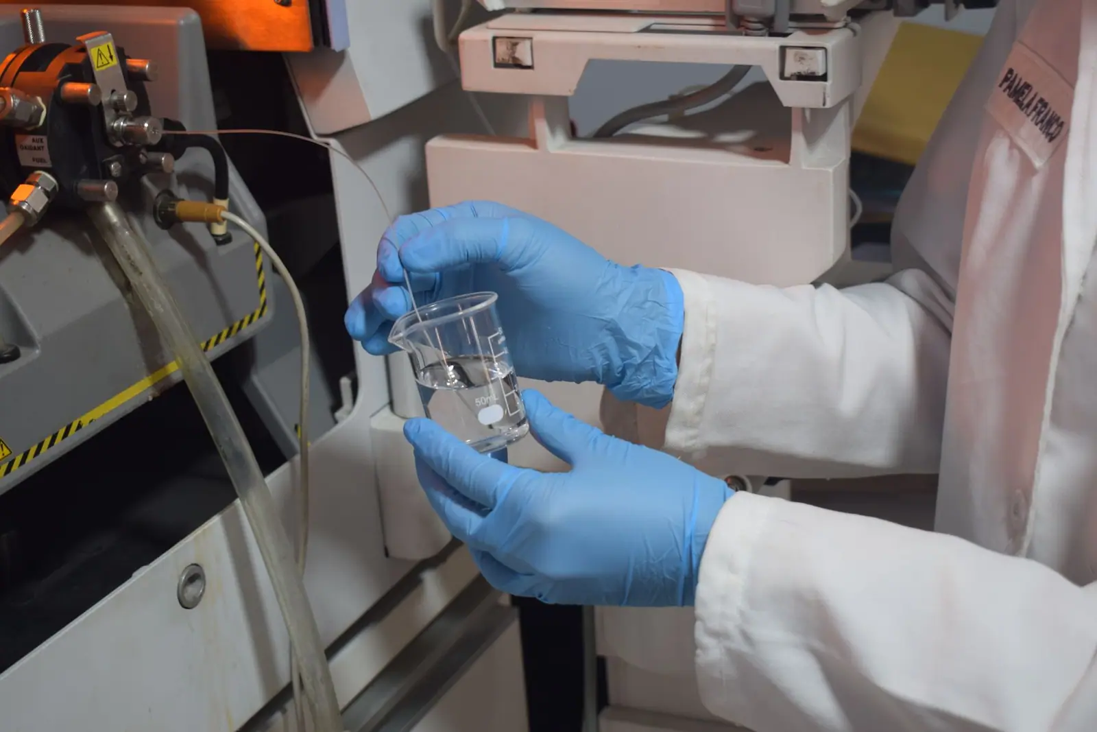 A gloved hand holding a laboratory beaker