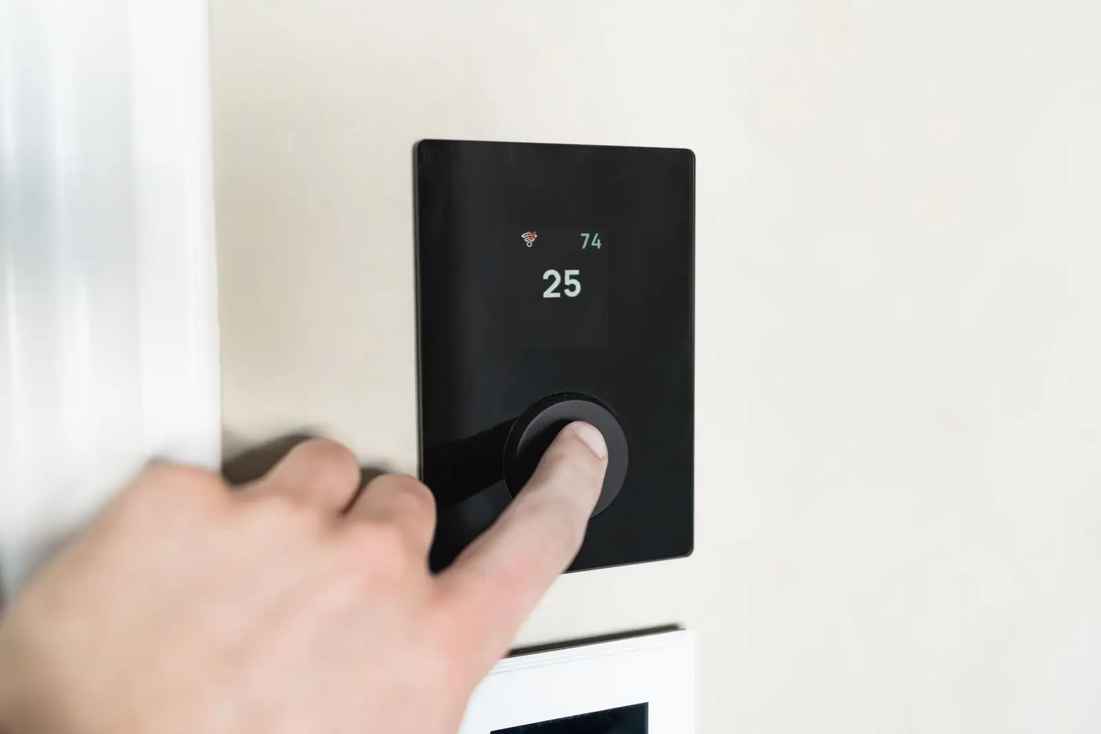 A hand adjusting a wall-mounted thermostat
